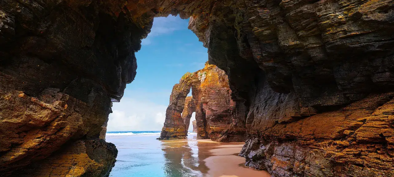 Arco natural en las calas de Lugo, con el mar y el cielo azul de fondo.