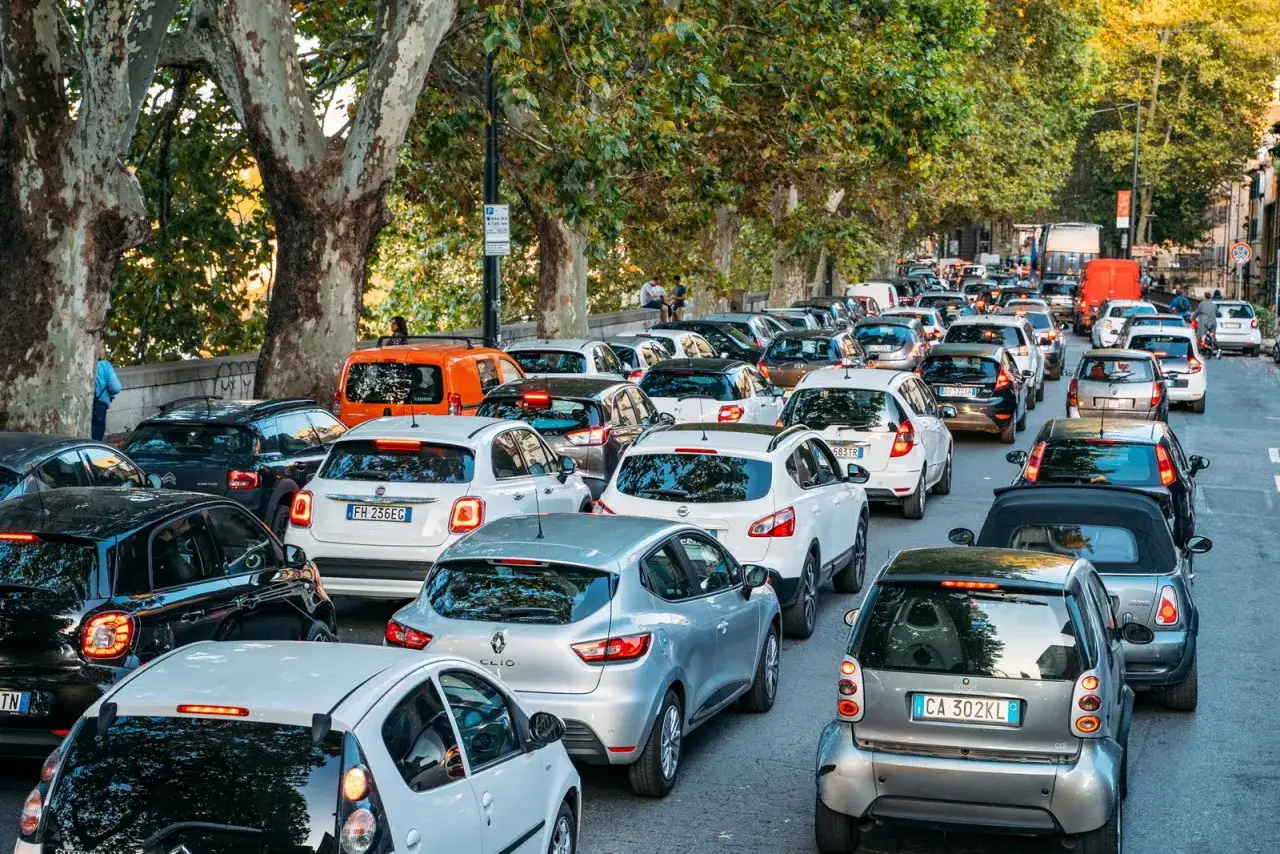 Traffico intenso con molte city car diesel incolonnate su una strada alberata.