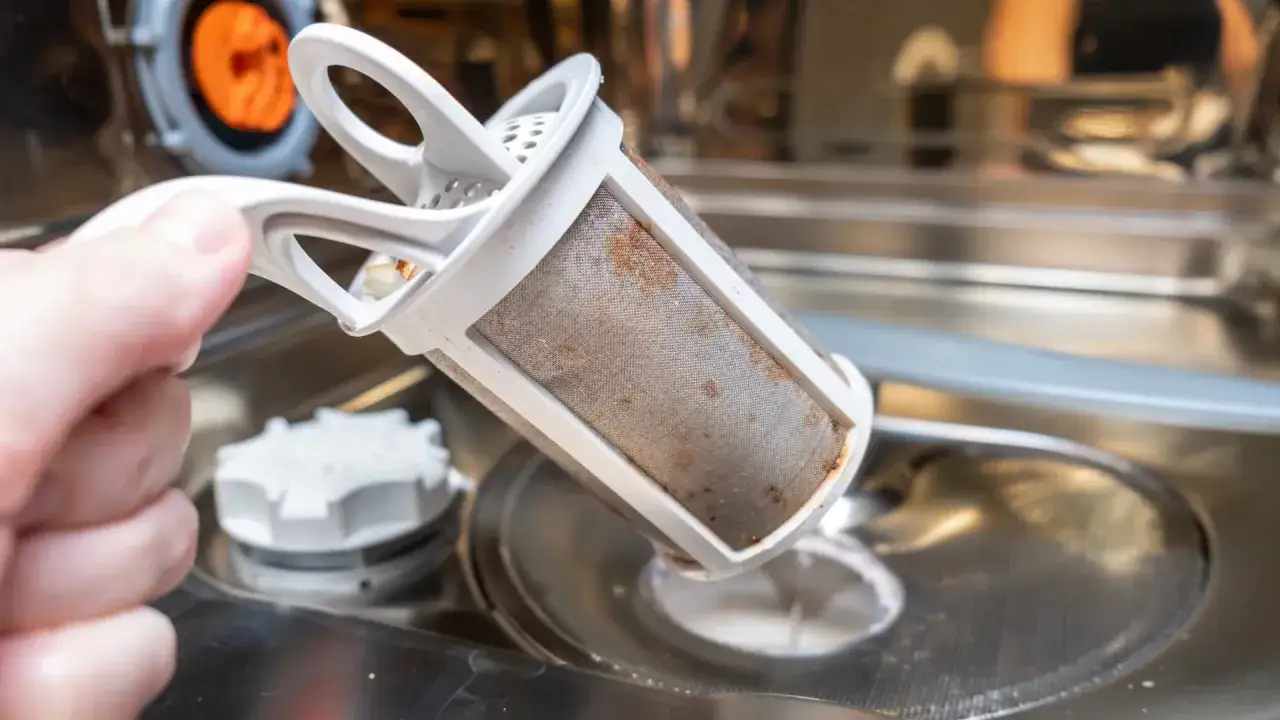 A hand removes a dirty dishwasher filter, a key step in how to fix a clogged dishwasher.