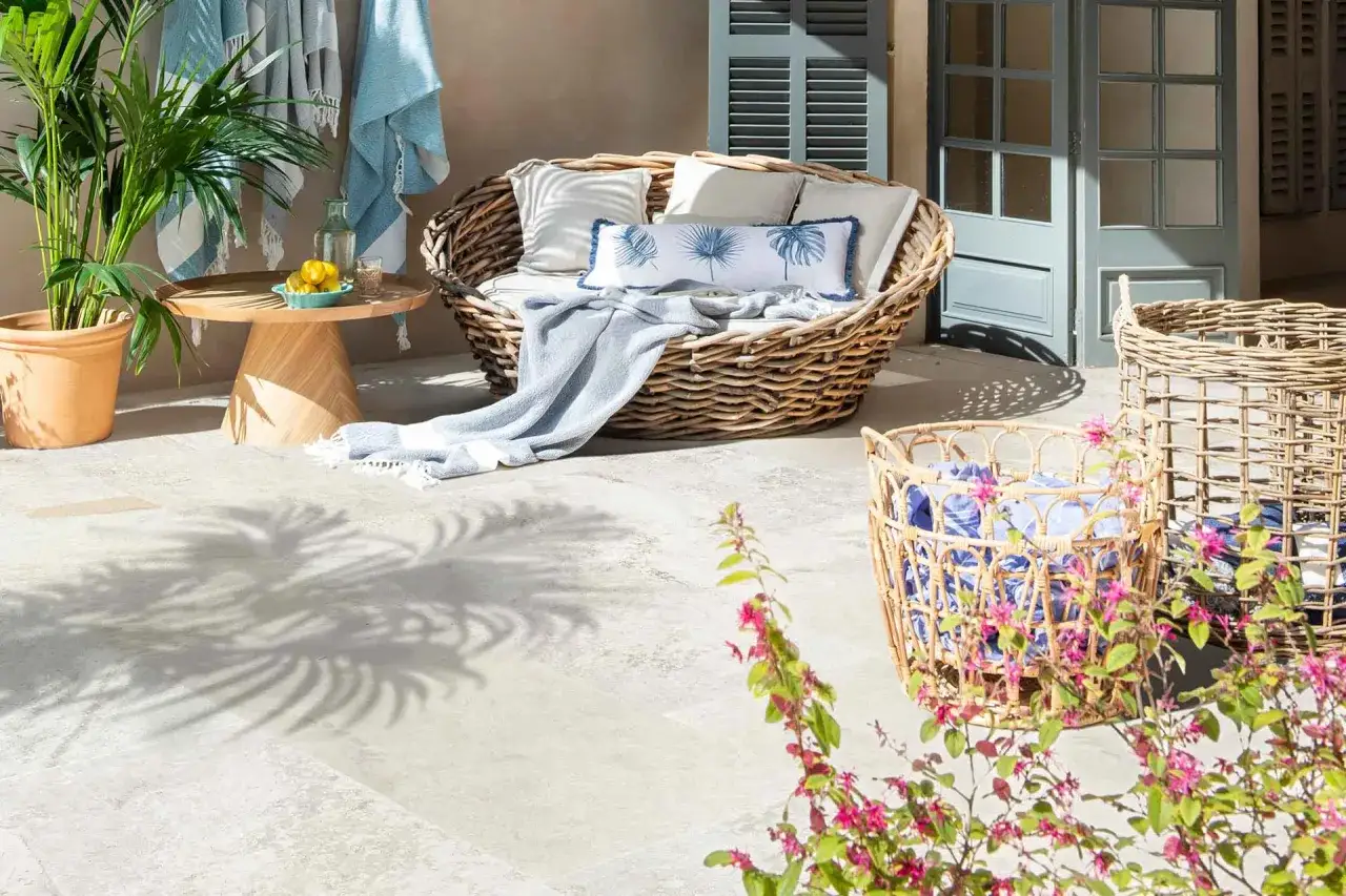C&oacute;moda terraza cubierta piso con sill&oacute;n de mimbre, mesa auxiliar de madera, plantas y cestas.