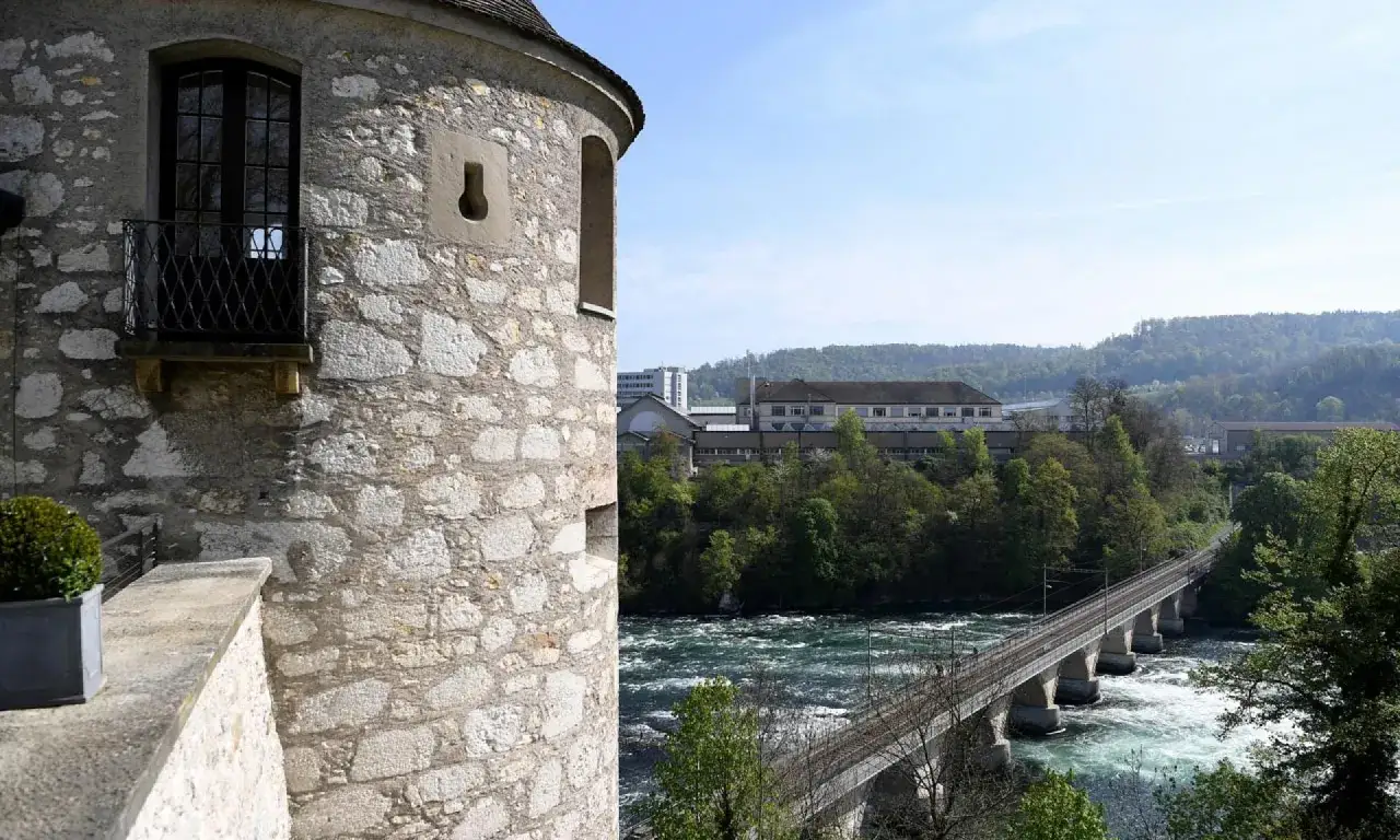 Alter Turm am Rheinfall, mit Blick auf die tosende Strömung und die Eisenbahnbrücke. Ein malerischer Eintritt ins Naturschauspiel.