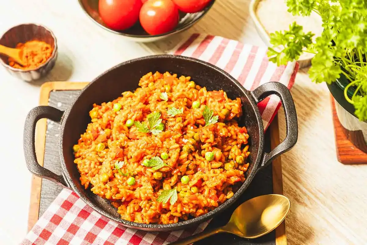 Herzhafter Djuvec Reis mit Erbsen und Tomaten, garniert mit Petersilie, serviert in einer Gusseisenpfanne.