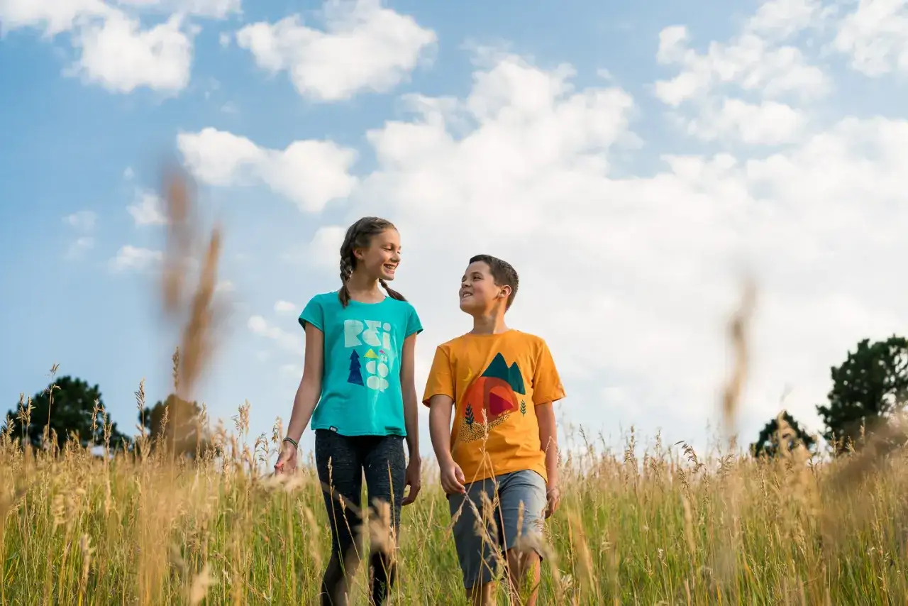 Two kids walk through a field of tall grass. A 50mm lens is good for capturing portraits like this, with a natural perspective and soft background blur.
