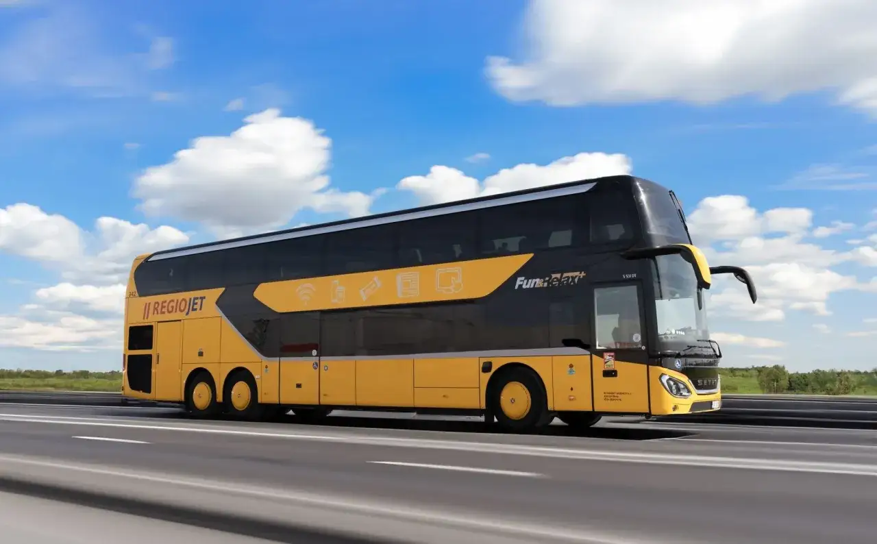Żółty autokar piętrowy RegioJet jedzie autostradą. Praga Warszawa to popularna trasa.