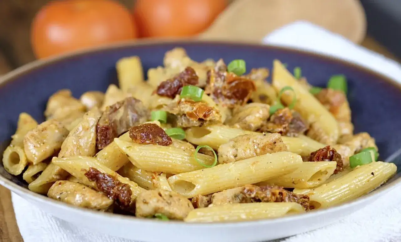 Penne z kurczakiem i suszonymi pomidorami, posypane szczypiorkiem, w kremowym sosie. Pyszne danie na obiad.