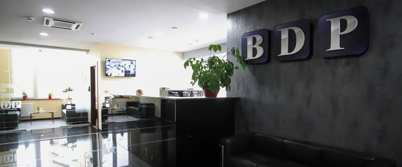 Nowoczesne biuro z recepcją, kanapami i logo BDP na ścianie.
