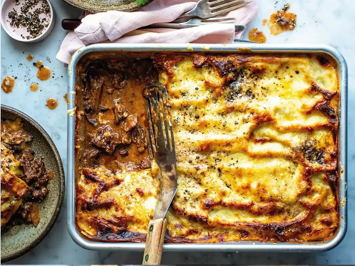 En stor ugnsform med en halväten lasagne, perfekt för lasagnens dag. En gaffel sticker upp ur den köttfyllda halvan.