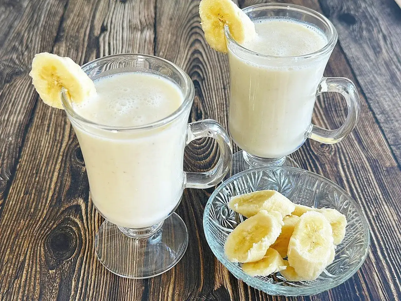Dwa pyszne koktajle bananowe w szklankach, ozdobione plasterkami banana. Obok miseczka z pokrojonymi bananami.