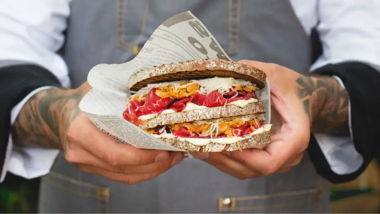 Kanapka z pastrami, chrzanem i kiszoną kapustą, zawinięta w gazetę. Pytasz pastrami co to? To pyszne, wędzone i peklowane mięso wołowe.