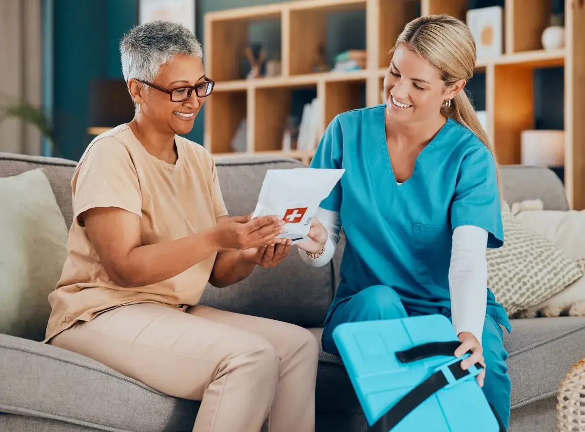 Pflegekraft richtet Medikamente und verabreicht sie einer Patientin. Sie l&auml;cheln sich an, w&auml;hrend die Medikamentenverpackung &uuml;bergeben wird.