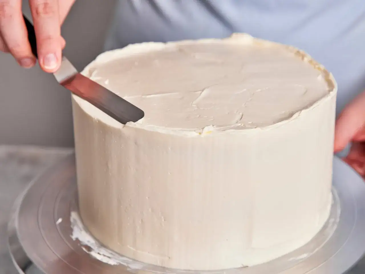 Eine Hand gl&auml;ttet mit einem Spachtel die Buttercreme auf einem Kuchen. Perfekt f&uuml;r ein Rezept Buttercreme ohne Pudding.