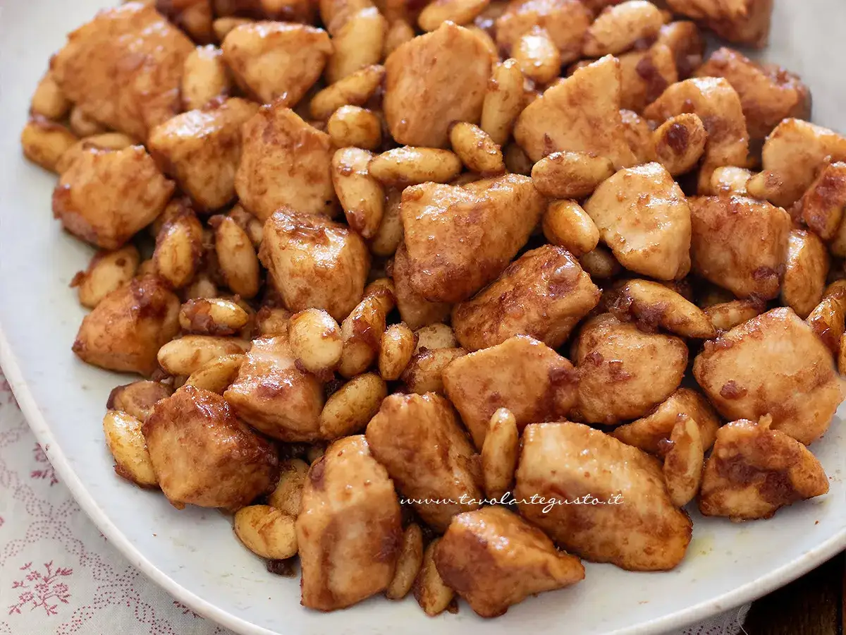 Un invitante pollo alle mandorle, con bocconcini dorati e mandorle tostate, servito su un piatto bianco.