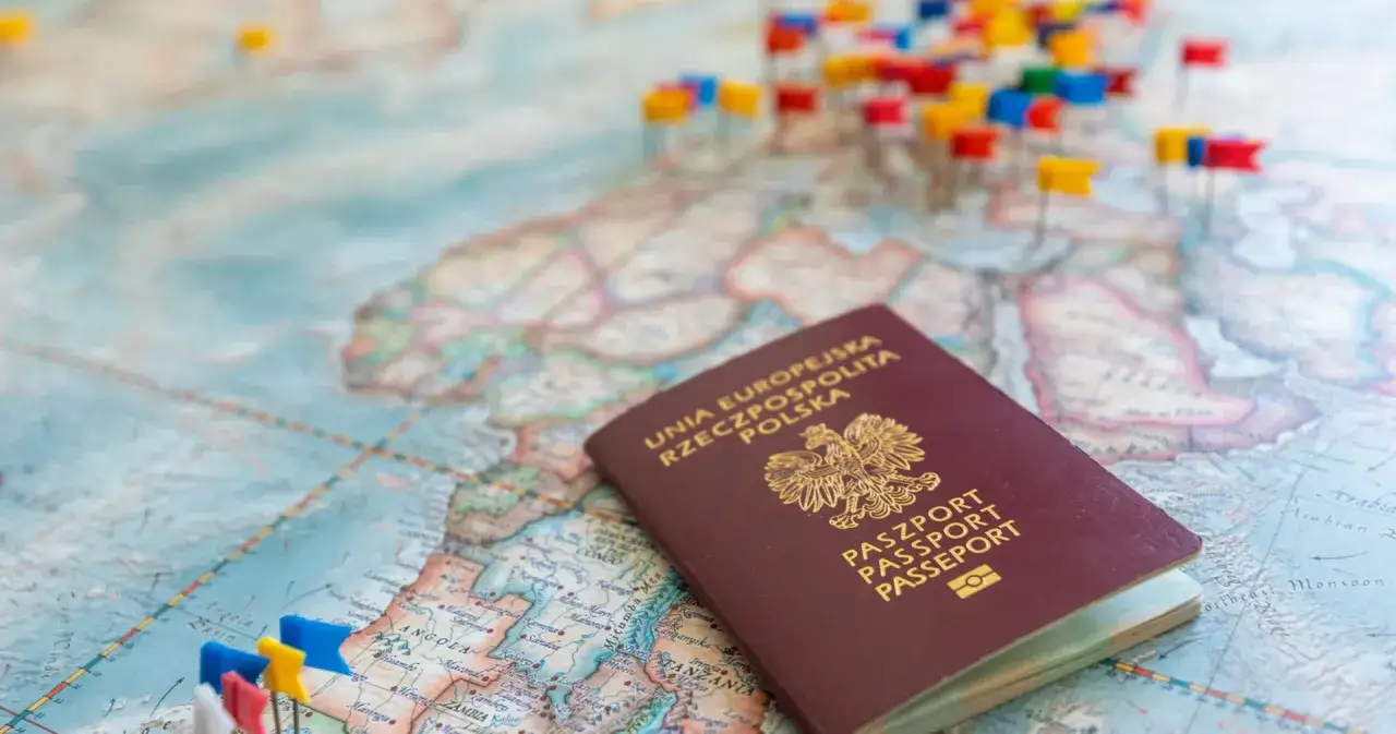 Polski paszport leży na mapie świata, gdzie bez paszportu nie wybierzesz się w podróż. Kolorowe chorągiewki oznaczają miejsca do odwiedzenia.