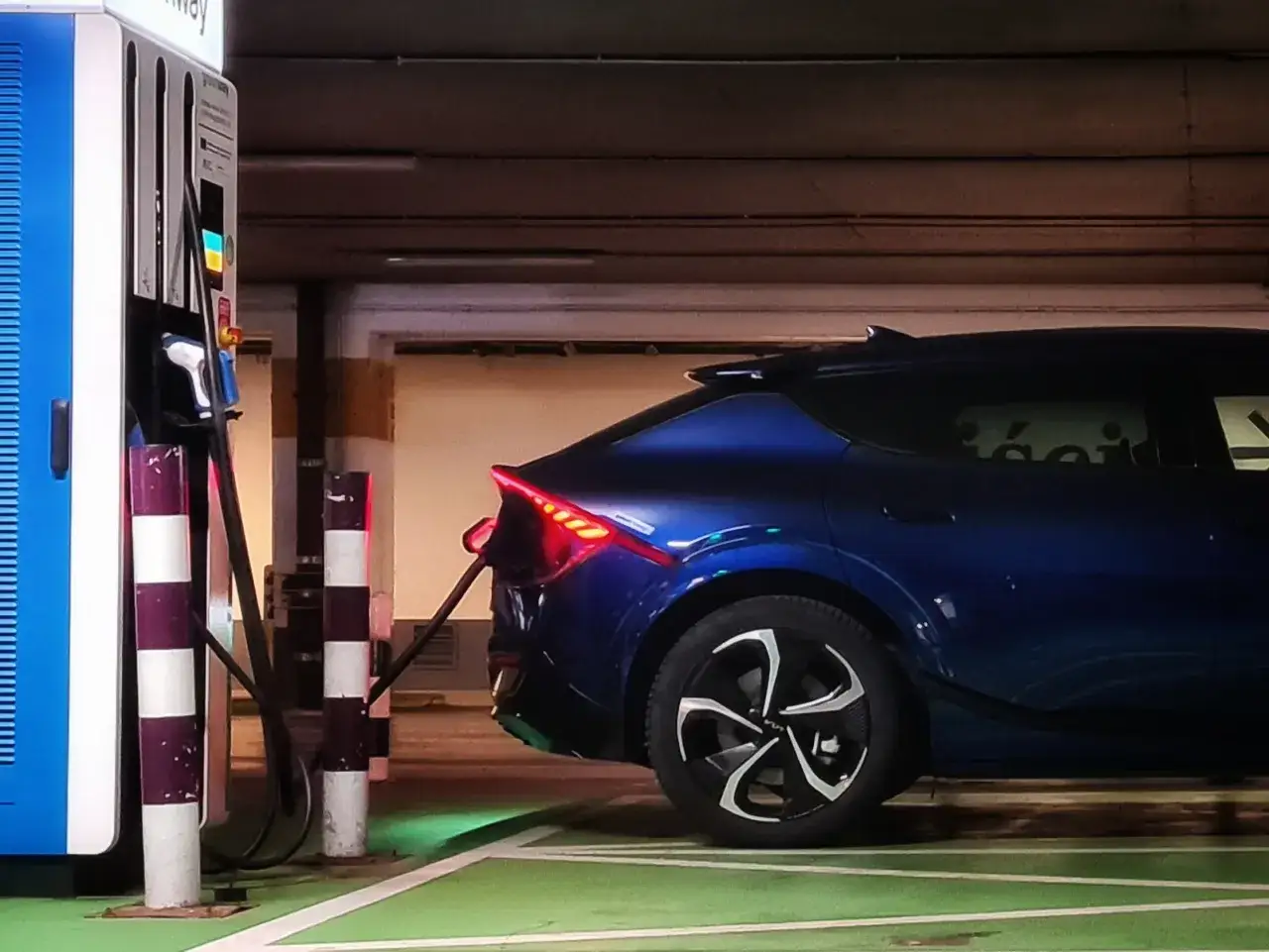 Niebieski samochód elektryczny ładuje się na parkingu. Zastanawiasz się, ile kosztuje ładowanie samochodu elektrycznego?