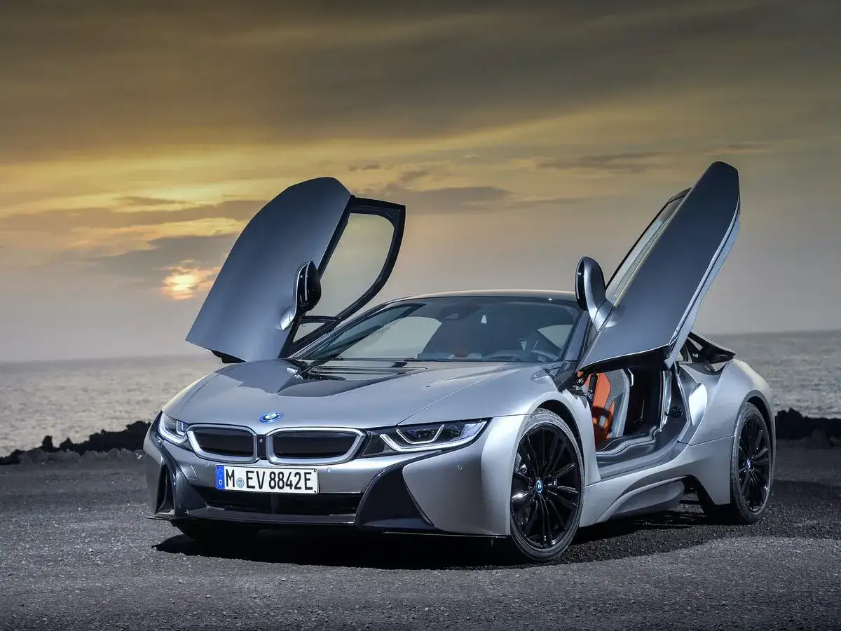 Srebrne BMW i8 z otwartymi drzwiami, zaparkowane nad morzem o zachodzie słońca. Sprawdź, jaka jest aktualna bmw i8 cena.