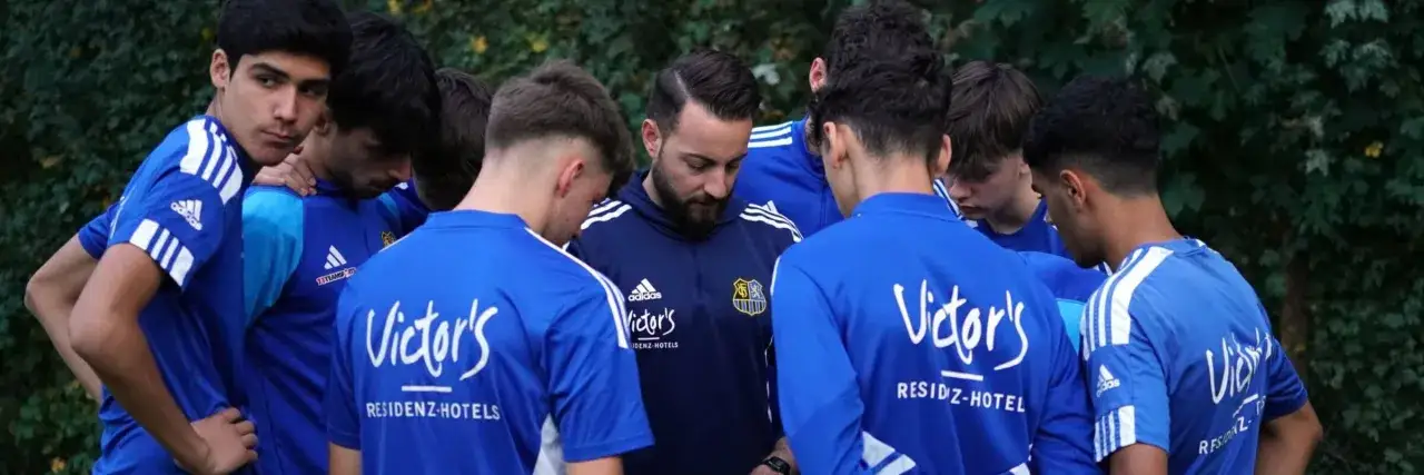 Jugendfu&szlig;baller im Kreis versammelt, Trainer spricht. Ein Moment der Konzentration vor dem n&auml;chsten Spiel.