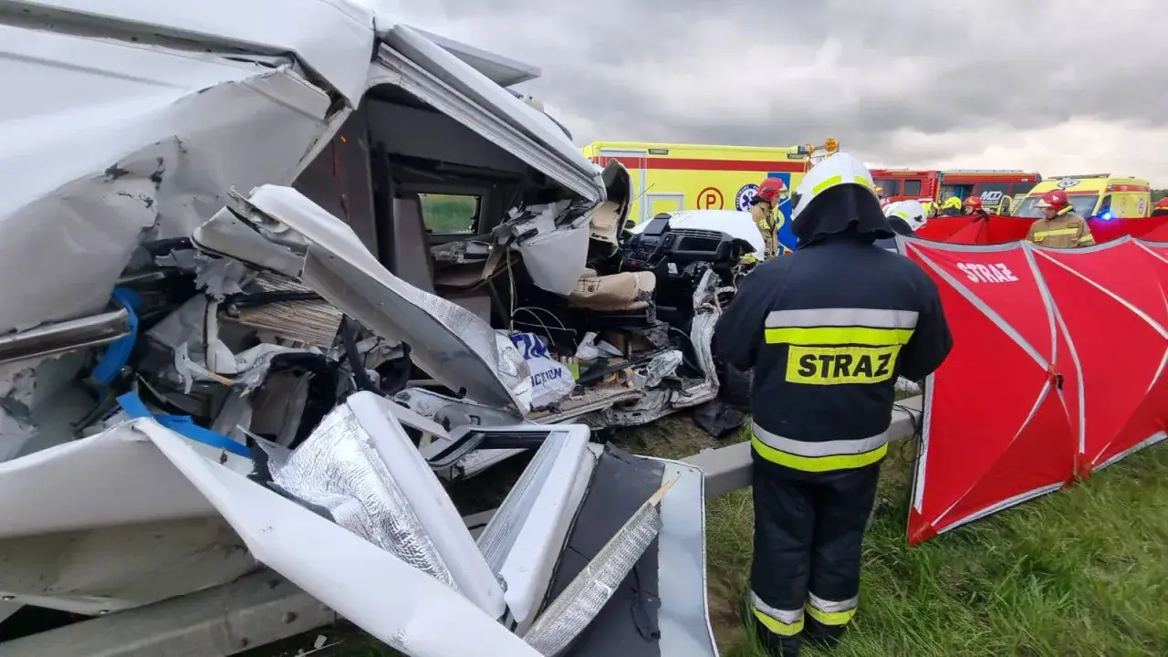 Strażacy zabezpieczają miejsce wypadku kampera. Pojazd jest mocno zniszczony, widoczne są wraki i wozy strażackie.