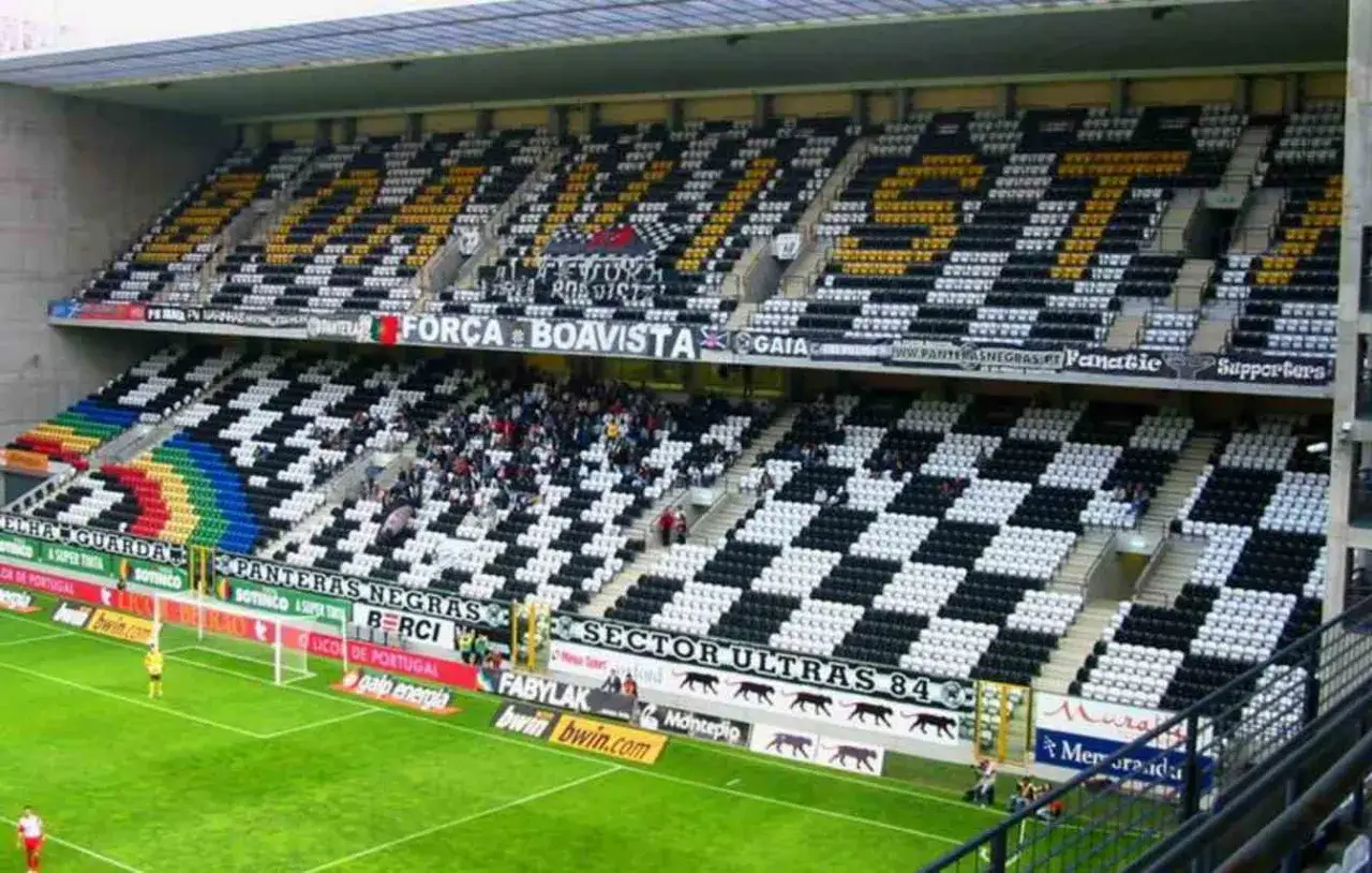 Stadion w Portugalii z trybunami w szachownicę. Kibice dopingują swoją drużynę, a na murawie widać piłkę.