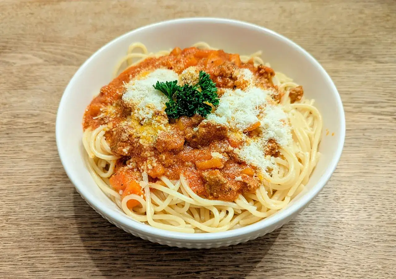 Misternie ułożone spaghetti z sosem bolognese, posypane parmezanem i natką pietruszki. Czy spaghetti bolognese jest zdrowe? Zależy od składników!