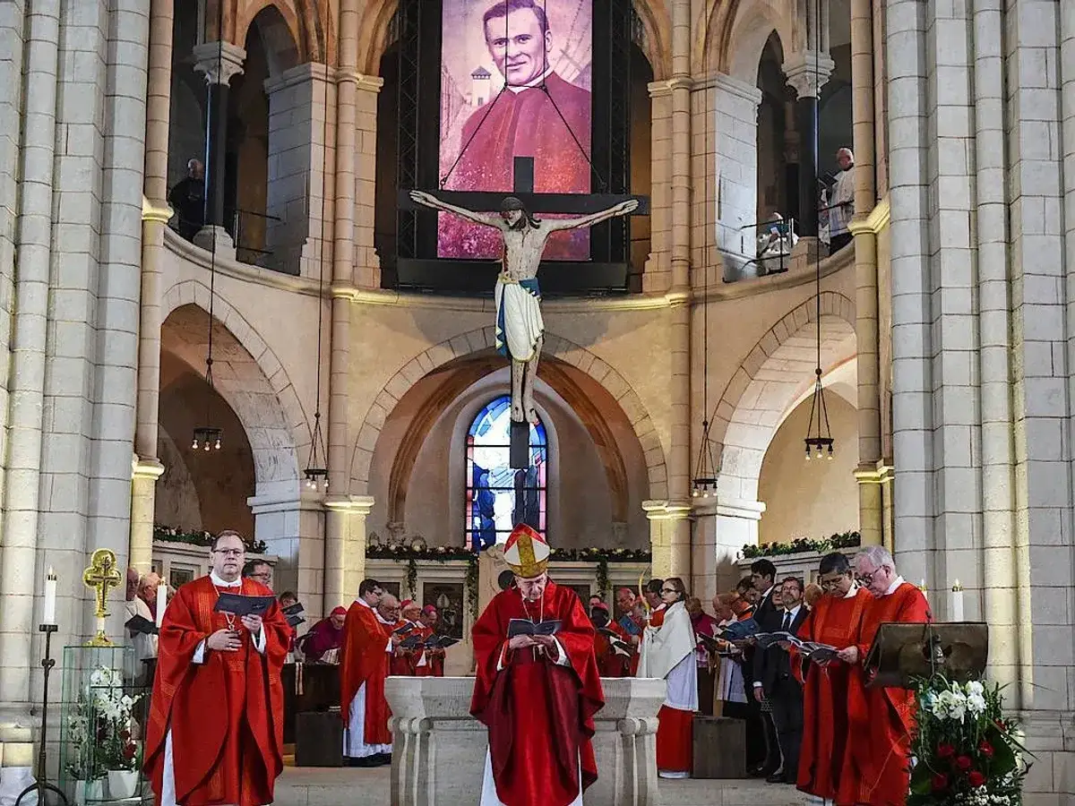 Feierlicher Gottesdienst mit Bischof Tebartz van Elst in rotem Ornat vor einem Kruzifix und einem Portr&auml;t.