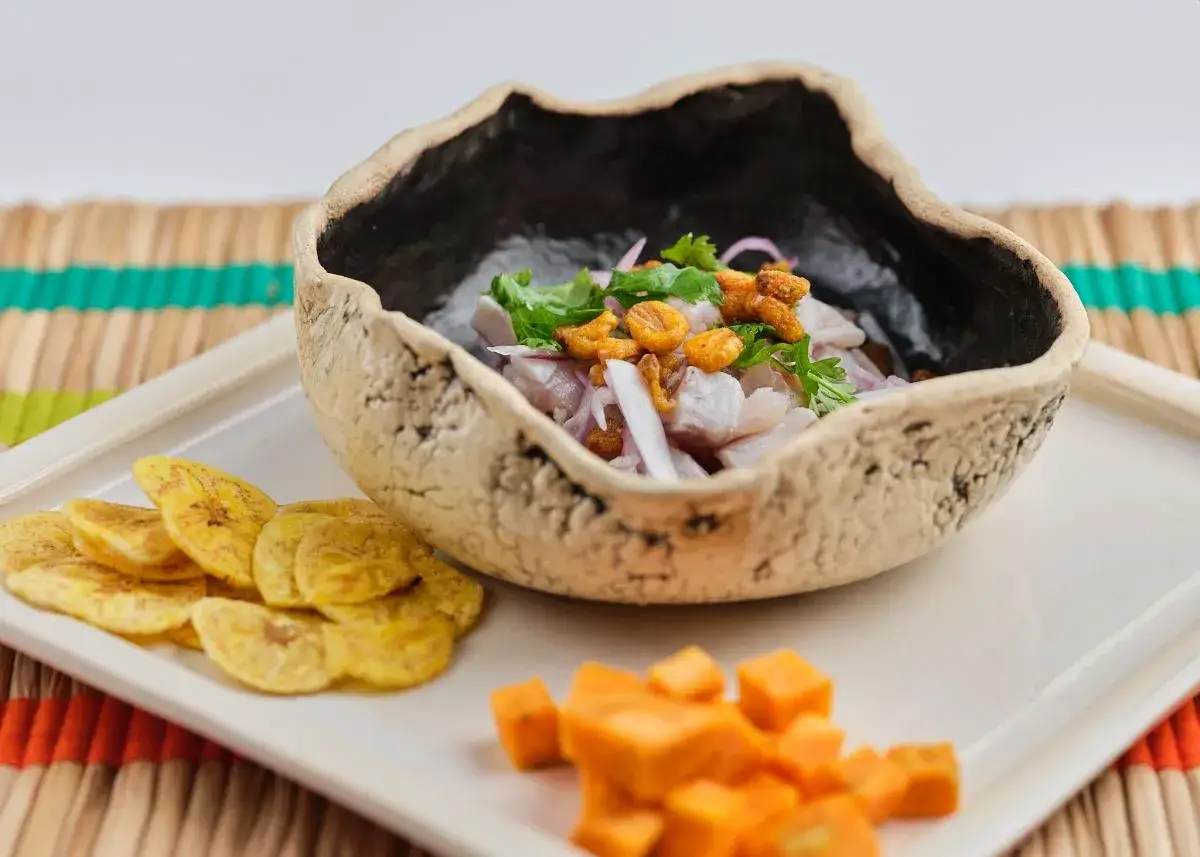 Delicioso ceviche de corvina fresco, servido en un cuenco rústico, acompañado de plátano frito y cubos de camote.