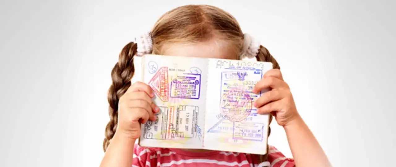 Dziewczynka z warkoczami trzyma paszport z pieczątkami. To przypomnienie, co jest potrzebne do odbioru paszportu dziecka.