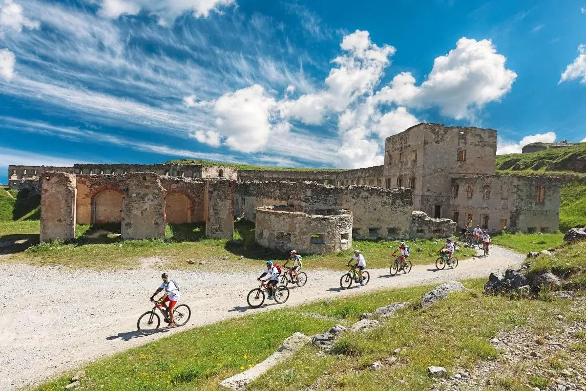 Ciclisti esplorano il **via del sale cammino** tra le rovine di un antico forte, sotto un cielo azzurro con nuvole bianche.