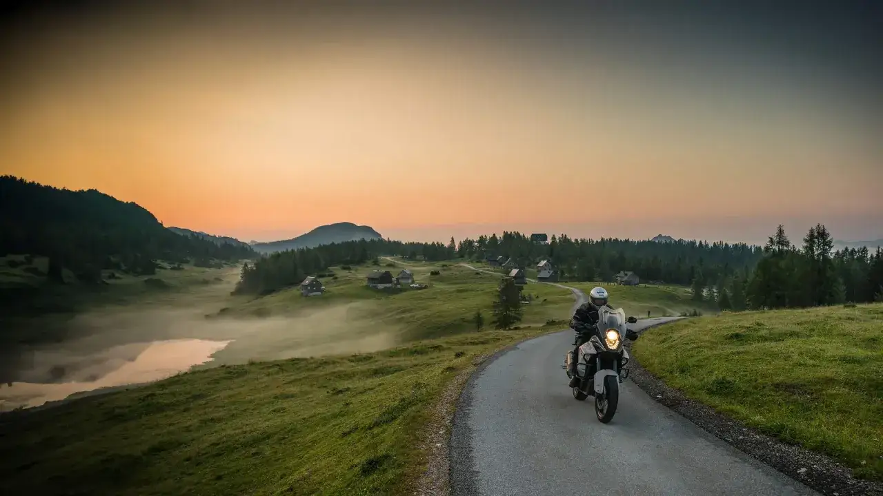 Motocyklista przemierza malownicze trasy motocyklowe w Austrii o wschodzie słońca, mijając górskie chatki i mglistą dolinę.