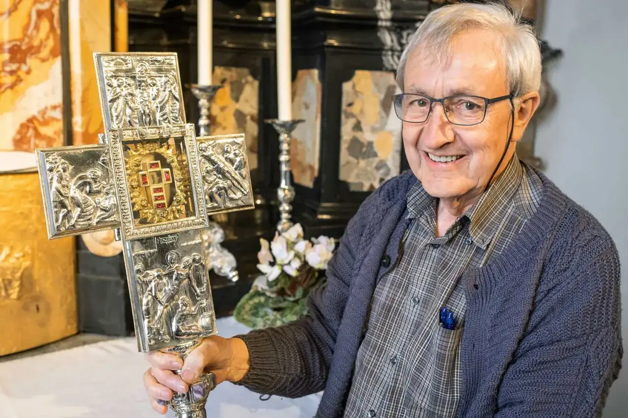 Ein Mann hält ein kunstvoll verziertes, silbernes Jesus-Kreuz-Original mit Reliefs und roten Steinen.