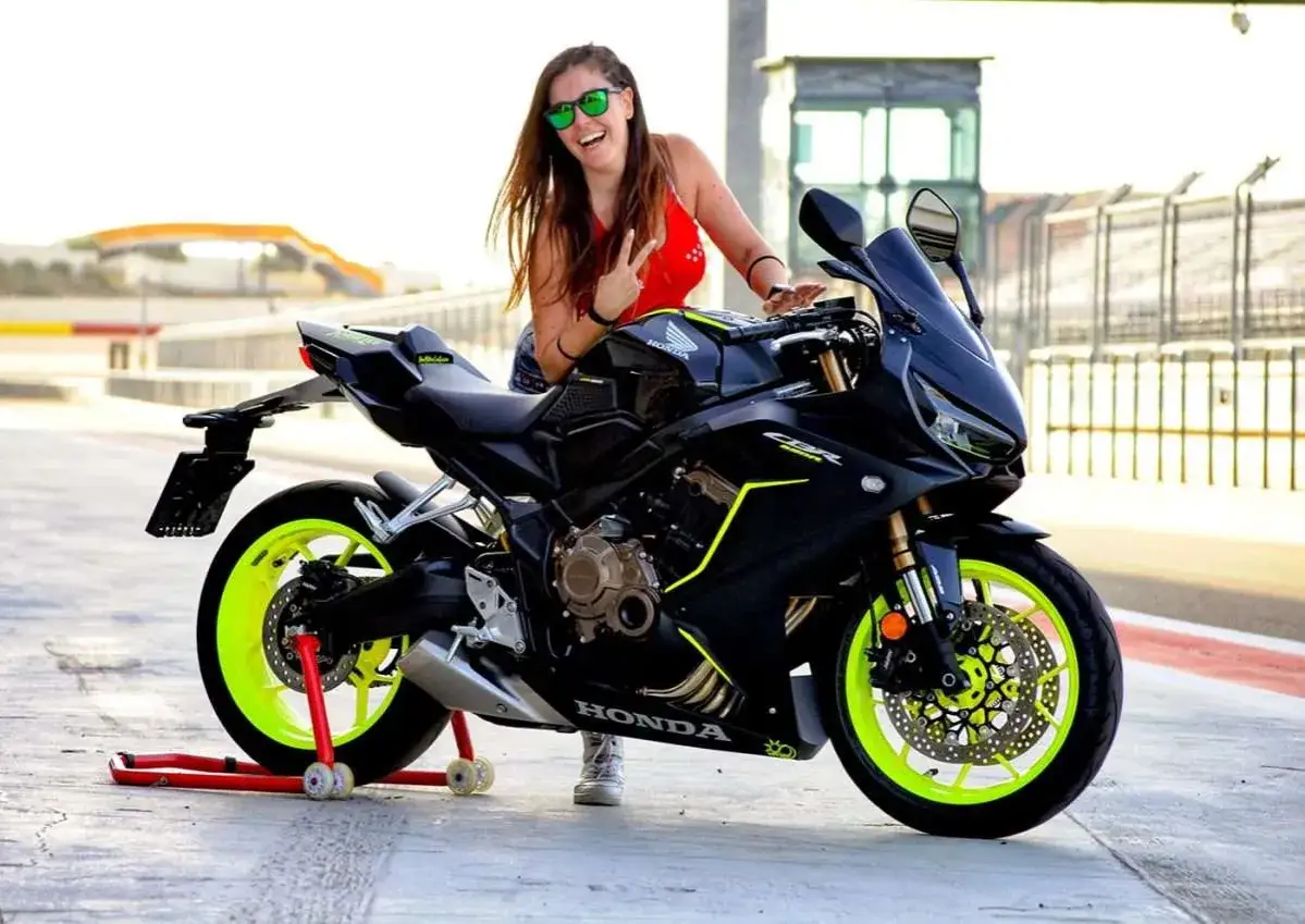 Chica sonriente con gafas verdes posa junto a una moto Honda CBR negra con detalles neón. ¡Perfecta para motos r para el a2!