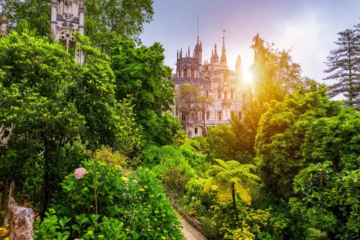Sintra Garten mit einem märchenhaften Schloss im Hintergrund, umgeben von üppigem Grün und Sonnenstrahlen.