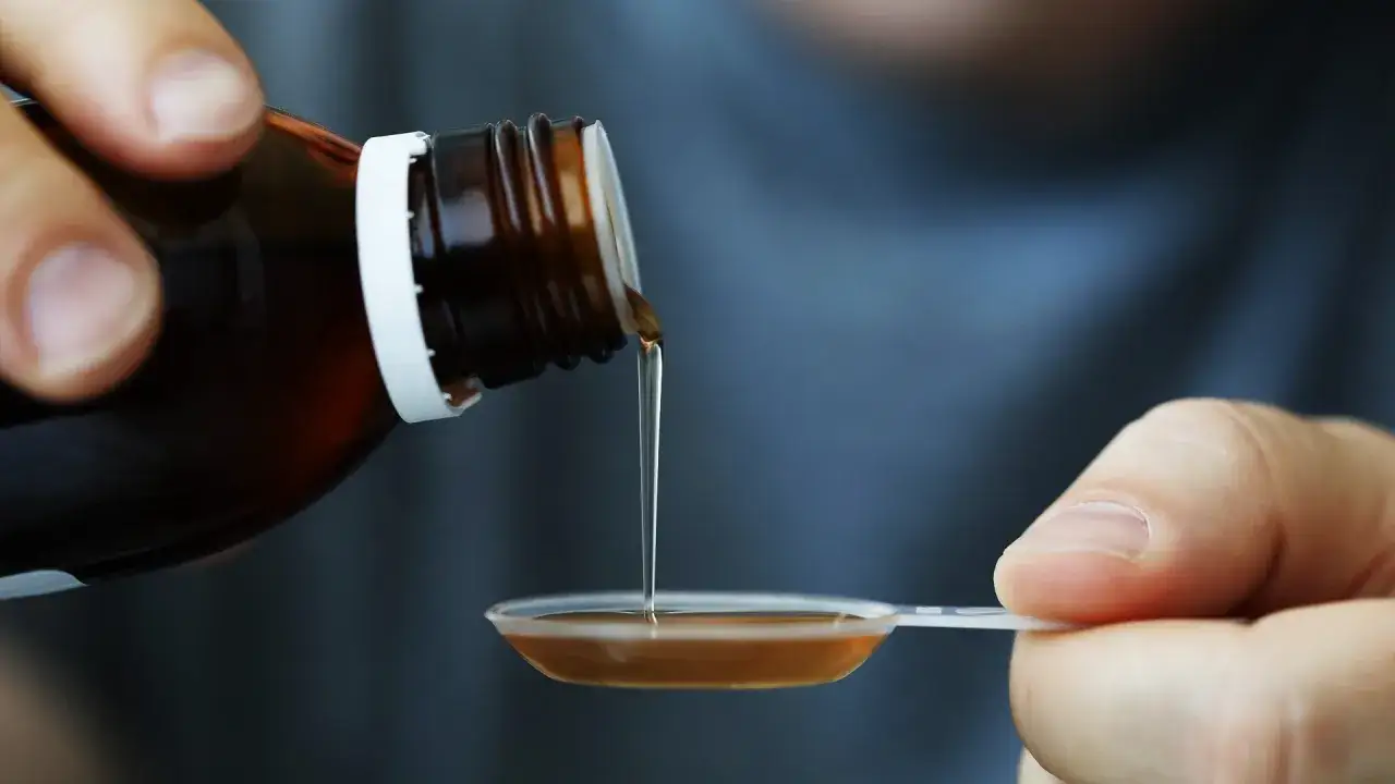Dłoń przelewa brązowy syrop glukozowy z butelki do plastikowej łyżeczki.