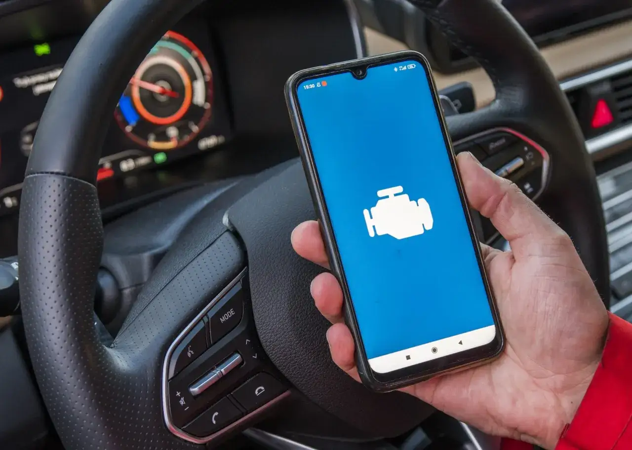Ręka trzyma smartfon z ikoną silnika, gotowy do diagnostyki auta. To najlepsza aplikacja OBD2 na Androida do monitorowania stanu pojazdu.