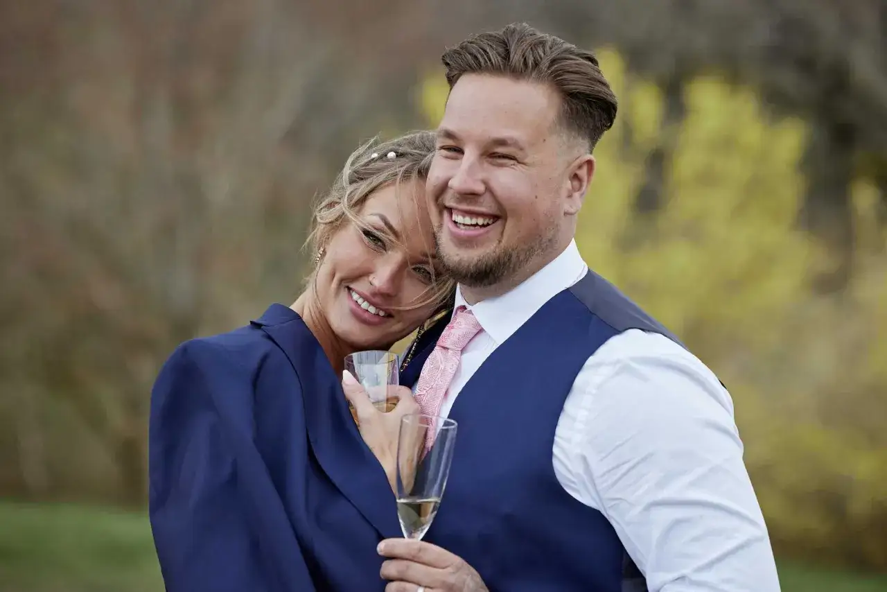 Ett lyckligt par, Rasmus och hans kärlek från Love is Blind, skålar med champagne utomhus.