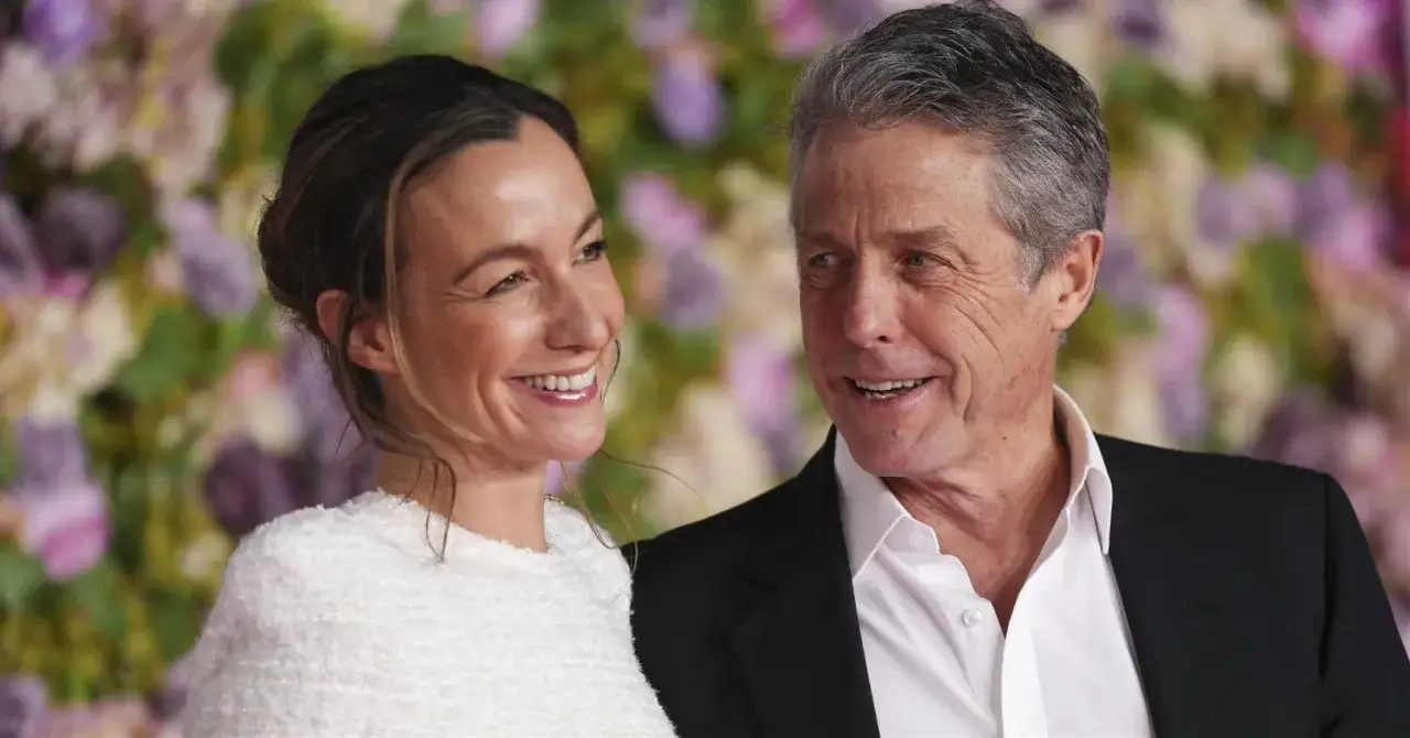 Uśmiechnięci Anna Eberstein i Hugh Grant pozują na tle kwiatów.
