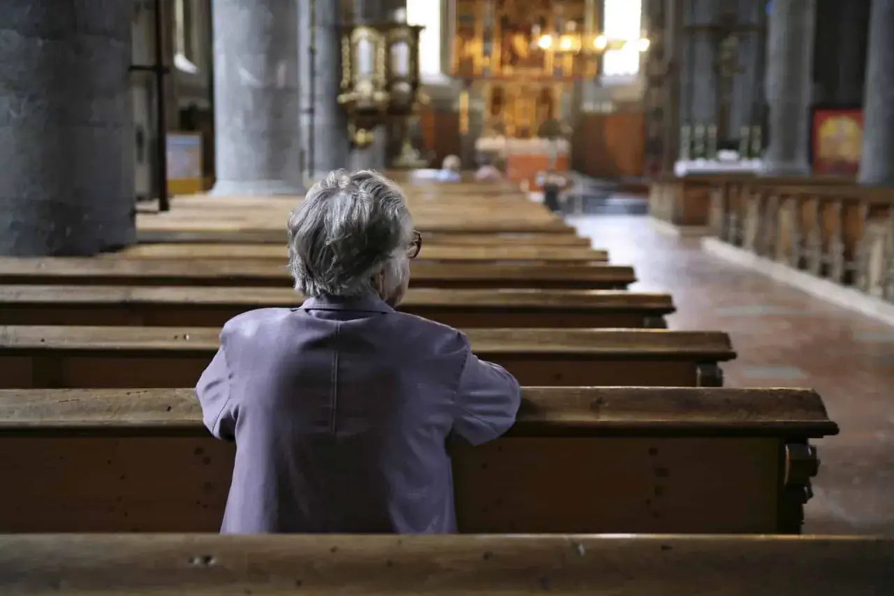Eine ältere Frau sitzt allein in einer Kirche. Vielleicht sucht sie Trost, wenn der Glaube nicht mehr passt.
