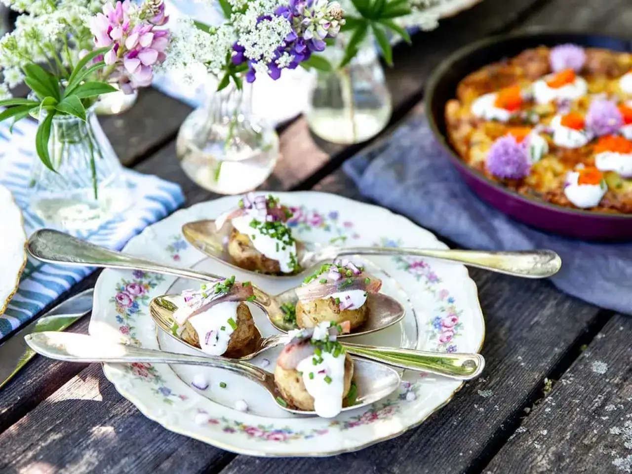 Sillunch midsommar på en vacker tallrik med potatis, gräddfil, rödlök och sill. Blommor i bakgrunden.