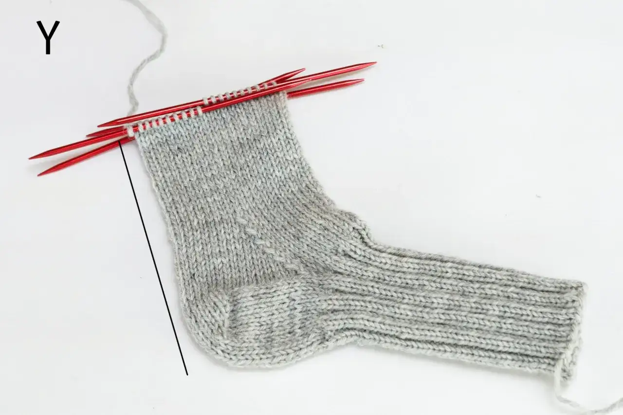 En grå stickad barnstrumpa på röda stickor. Perfekt för att sticka enkla sockor till barn.