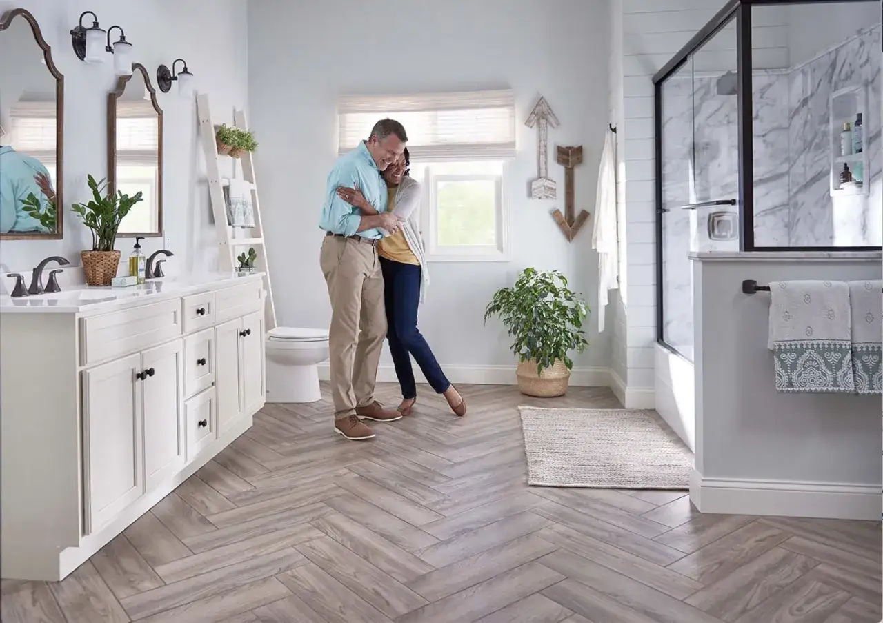 A couple embraces on a bathroom floor with a herringbone pattern, showcasing one of the many beautiful types of bathroom floor options.