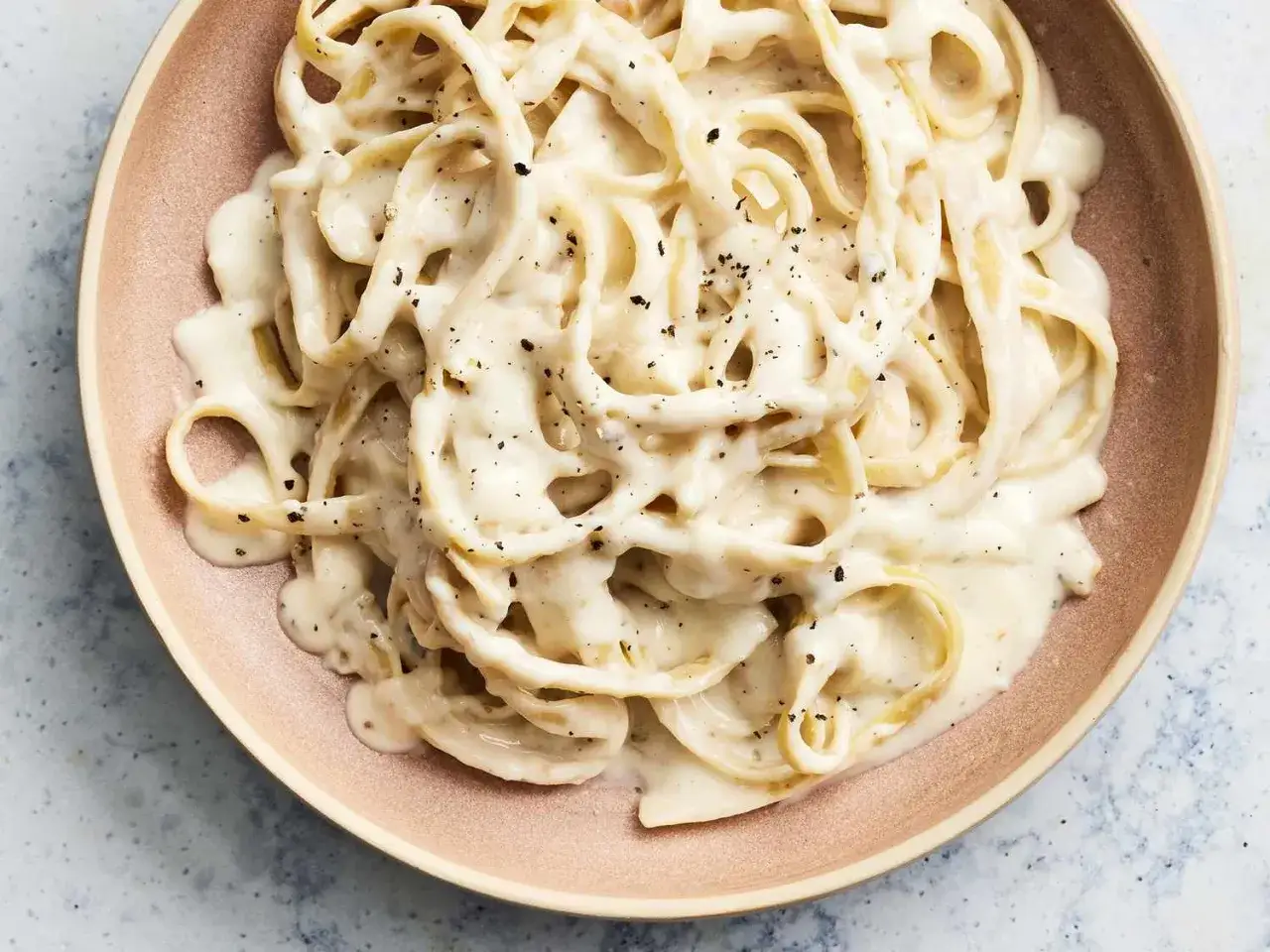 Krämig pasta alfredo med svartpeppar, serverad i en ljusrosa skål.