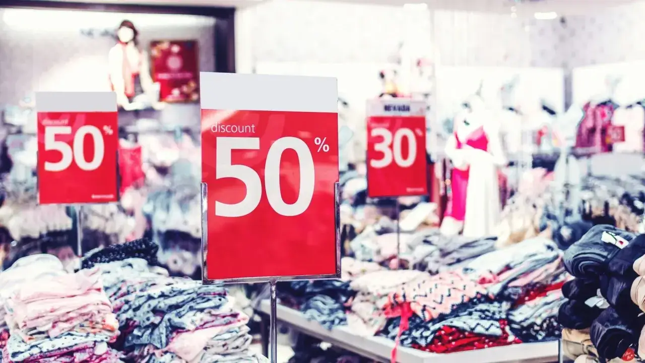Soldes d'été : pancartes rouges annonçant 50% et 30% de réduction sur des vêtements en magasin.