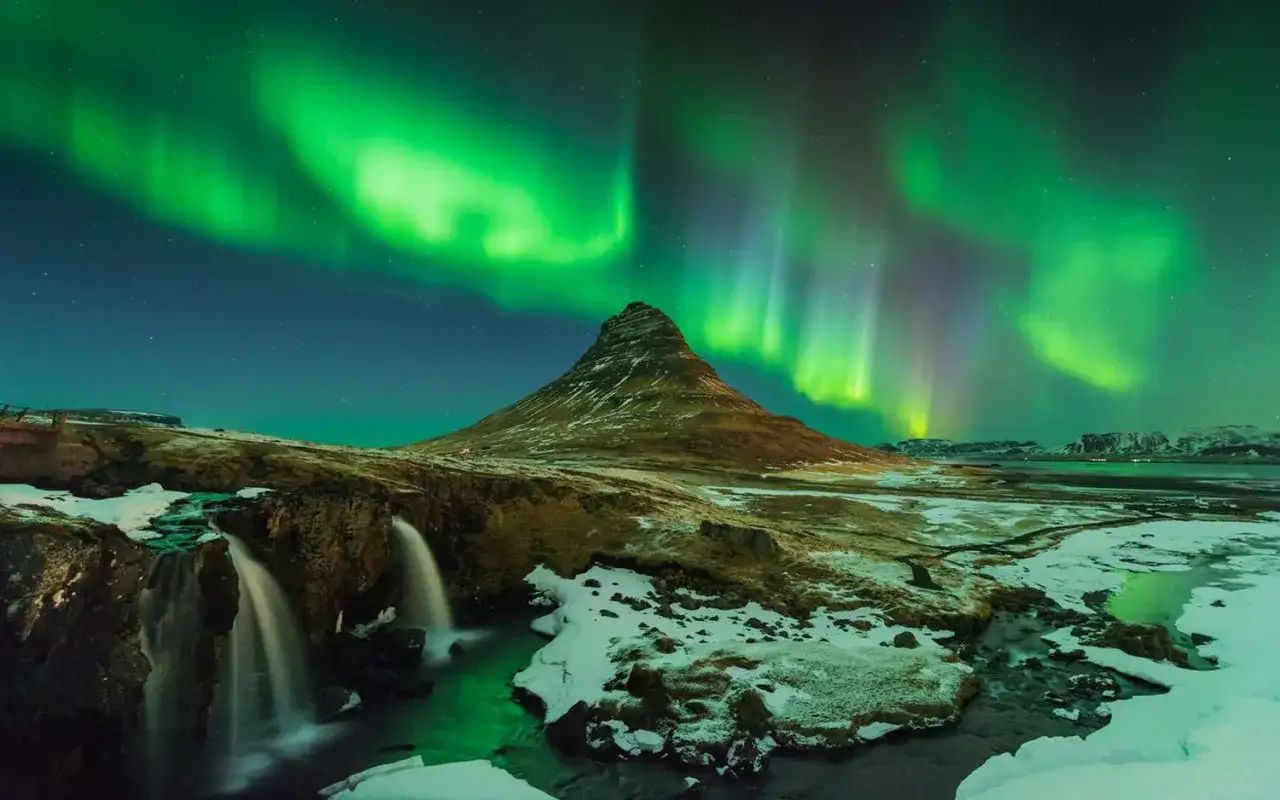 Spektakularna zorza polarna nad Islandią, z charakterystyczną g&oacute;rą Kirkjufell i wodospadem.