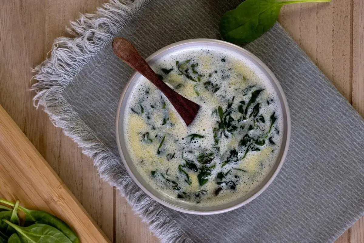 Sauce oseille grand chef, cr&eacute;meuse et onctueuse, garnie de feuilles d'&eacute;pinards frais. Une cuill&egrave;re en bois repose dans le plat.
