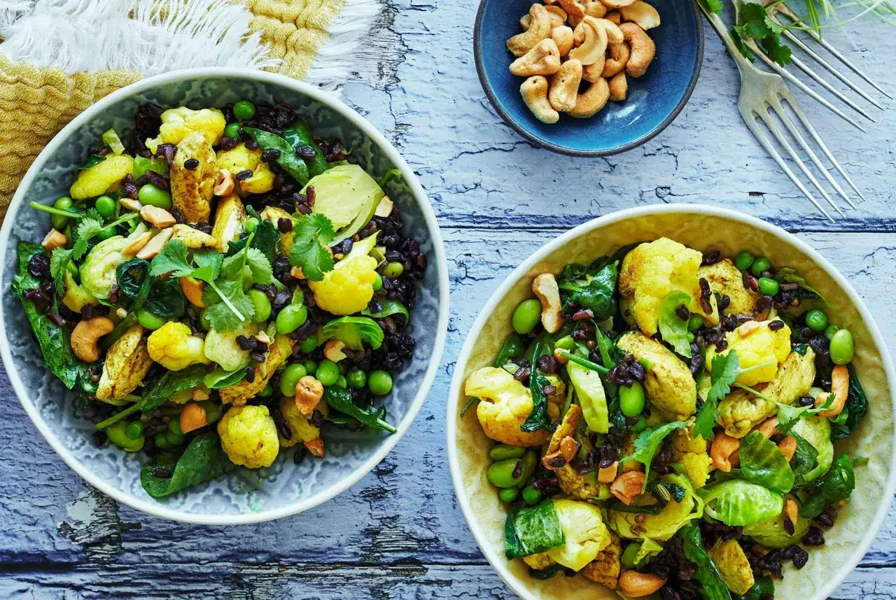 Två skålar med pilaffris kyckling, blomkål, gröna bönor och cashewnötter.