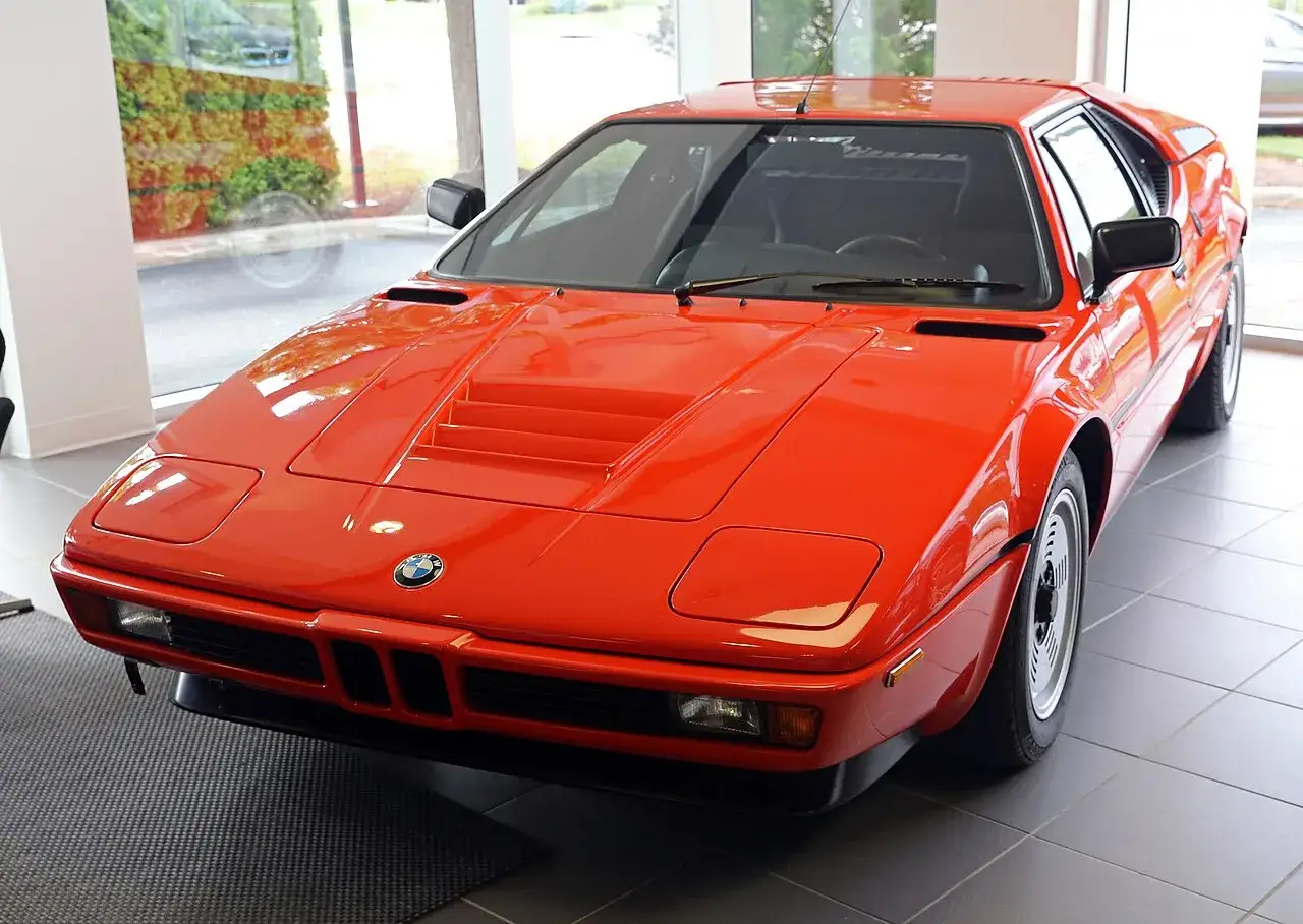 Pomarańczowy klasyk BMW E26 z lat 80. błyszczy w salonie, gotowy na jazdę.