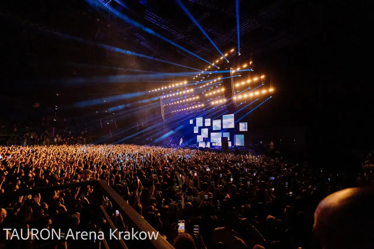Tłum ludzi na koncercie rapowania, oświetlony sceną i światłami. Jan rapowanie koncert w TAURON Arenie Krak&oacute;w.