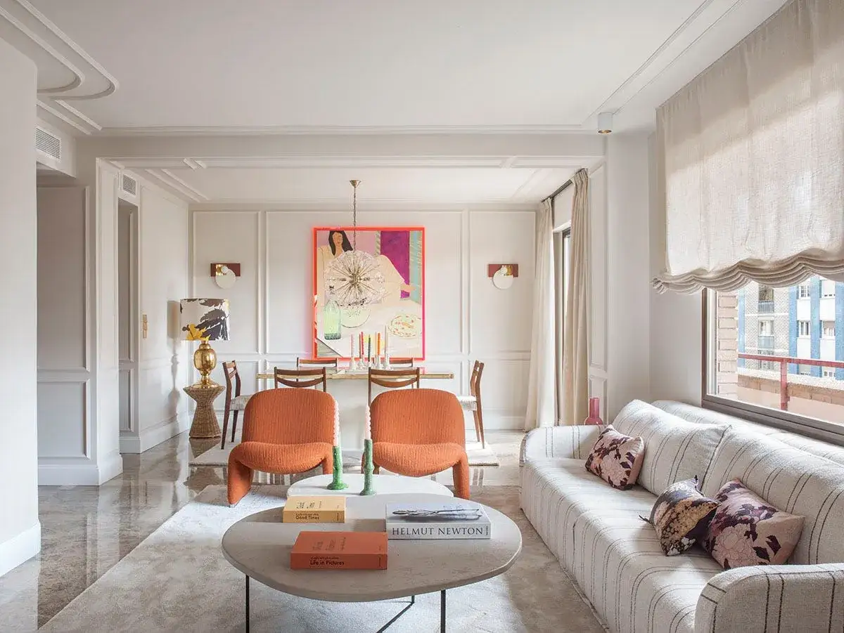 Ideas para como decorar un salón moderno y elegante: sofá curvo, butacas naranjas, mesa de centro redonda y arte vibrante.