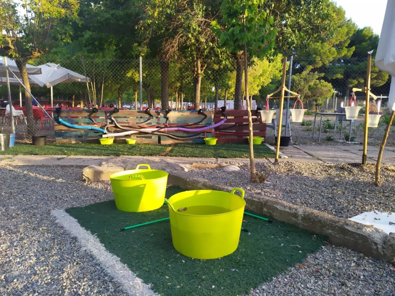 Un espacio de juego con un río de mangueras y cubos verdes, ideal para refrescarse y divertirse bajo el sol.