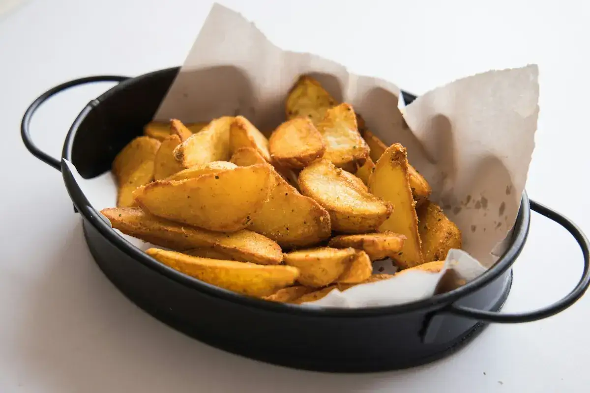 Klyftpotatis i airfryer, gyllene och krispiga, serverade i en svart skål med bakplåtspapper.