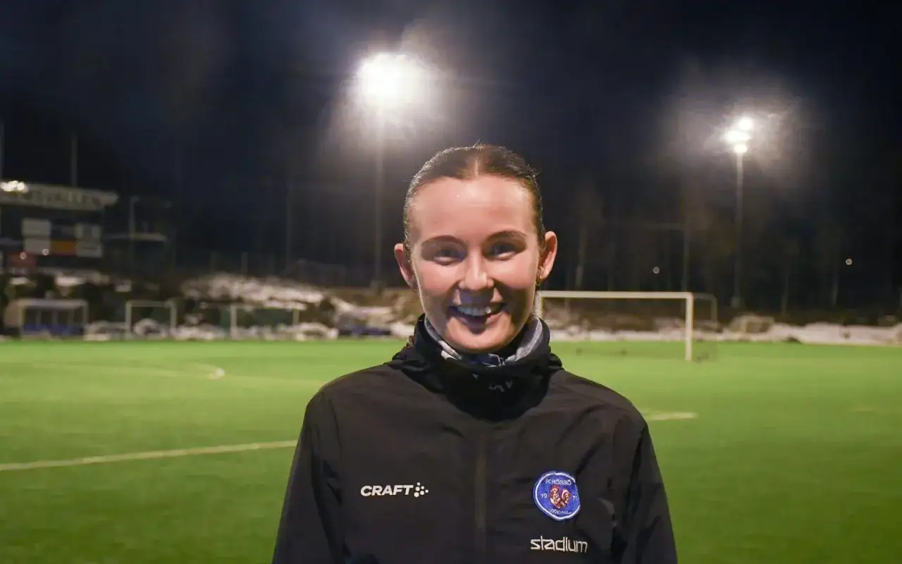 Evelina Persson ler mot kameran på en fotbollsplan i mörker, upplyst av strålkastare.